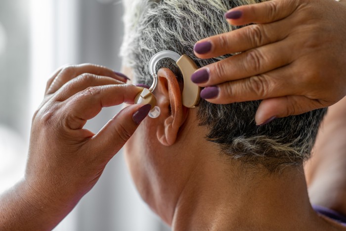 A woman of colour is placing a hearing aid on her ear.